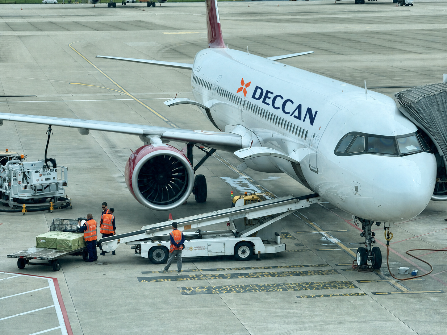 Airport team preparing cargo beside a Deccan-branded aircraft
